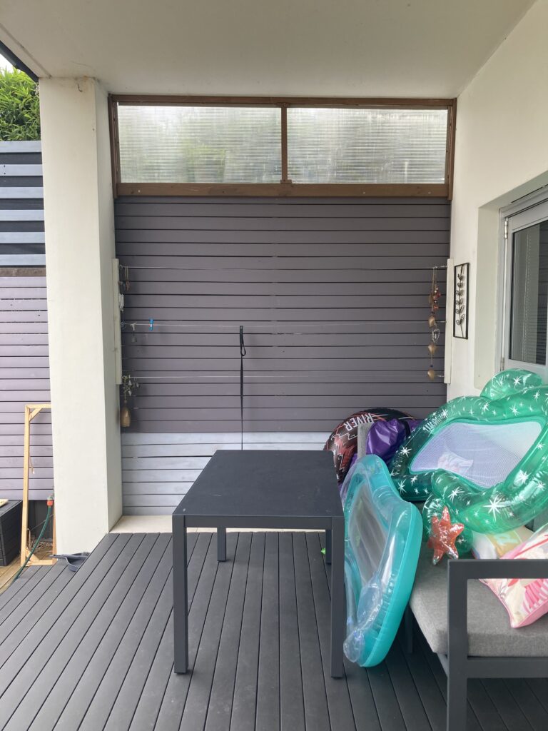 Before photo of the outdoor kitchen space showing a purple and blue wall with a large glass window on top and clothing lines.