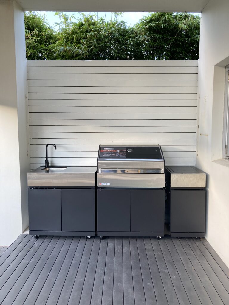 After photo of the outdoor kitchen featuring a painted white wall and modular kitchen will grill and sink