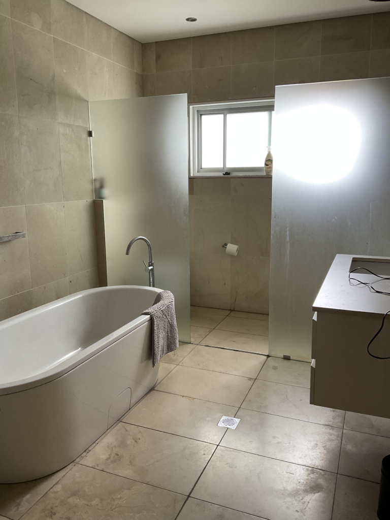 Before image of the bathroom renovation in Sydney from the doorway showing the full bathroom including the bathtub, two shower screens (one hiding the toilet) and vanity