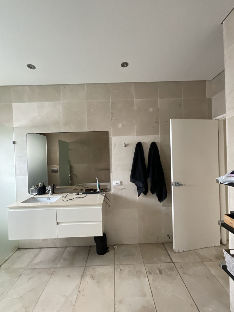 Before image of the bathroom renovation in Sydney showing the vanity wall with a vanity, large mirror and towels