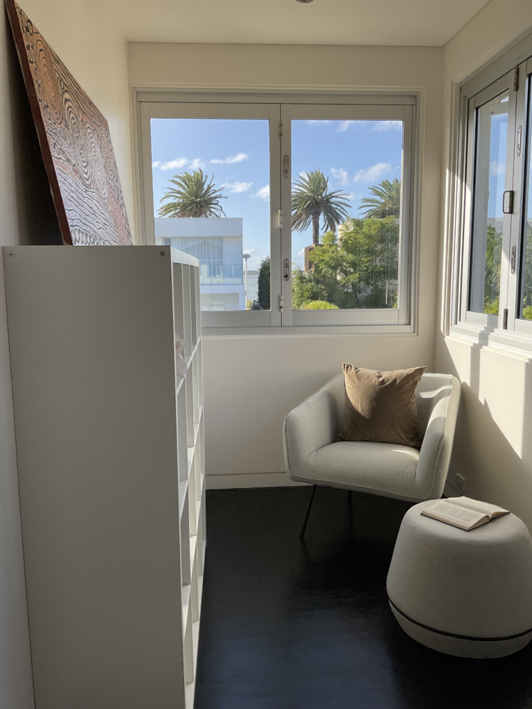 Sitting area of the 5th bedroom with bookshelves. Window shows palm trees and a view of Botany Bay