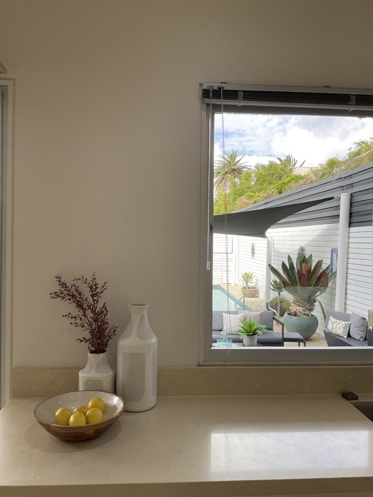 Kitchen bench with styling and the servery windows open showing an outdoor sitting area and the pool