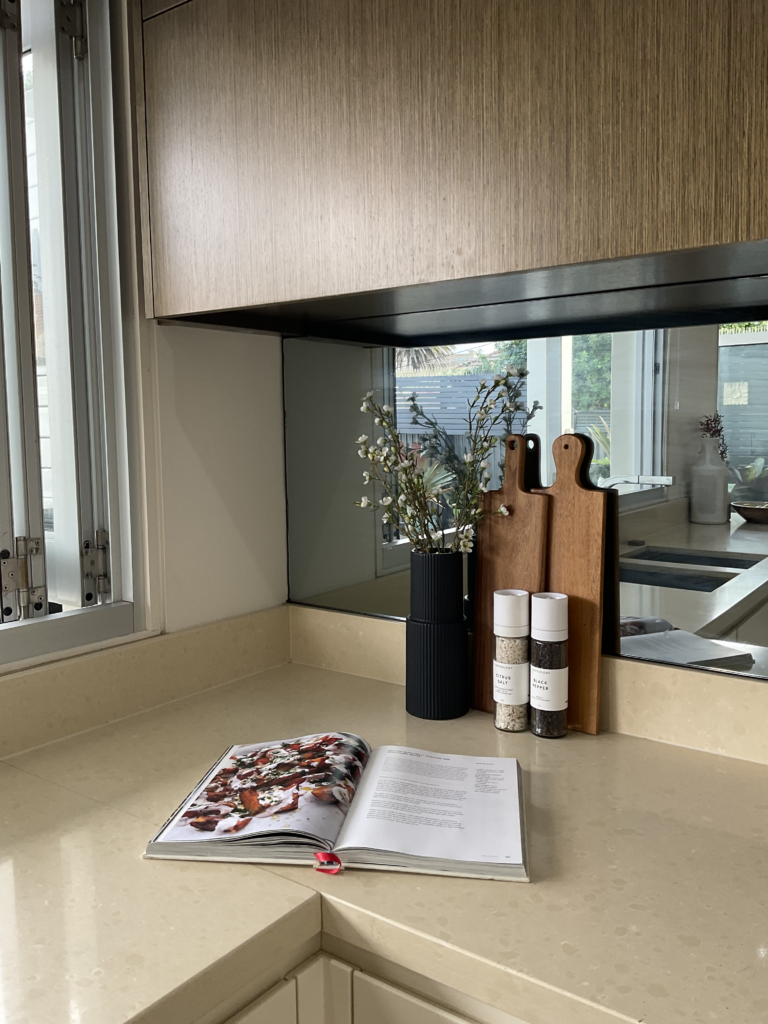 Styling shot of the kitchen bench with an open cookbook, vase, cutting boards and salt and pepper