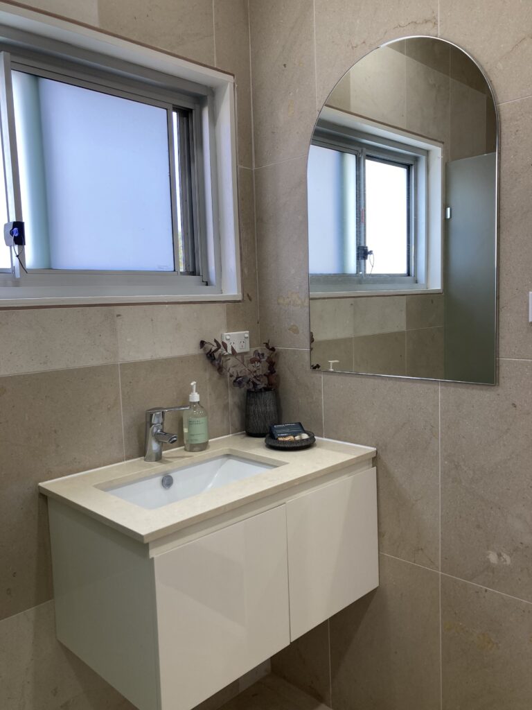 Ensuite for the main bedroom with a brand new mirror. Image shows a vanity with styling and a window above.