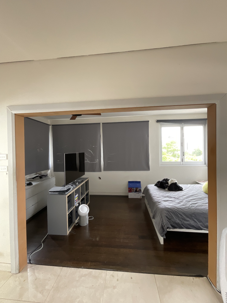 Opening of the former studio bedroom with a bed and paper blockout blinds covering the sunroom windows