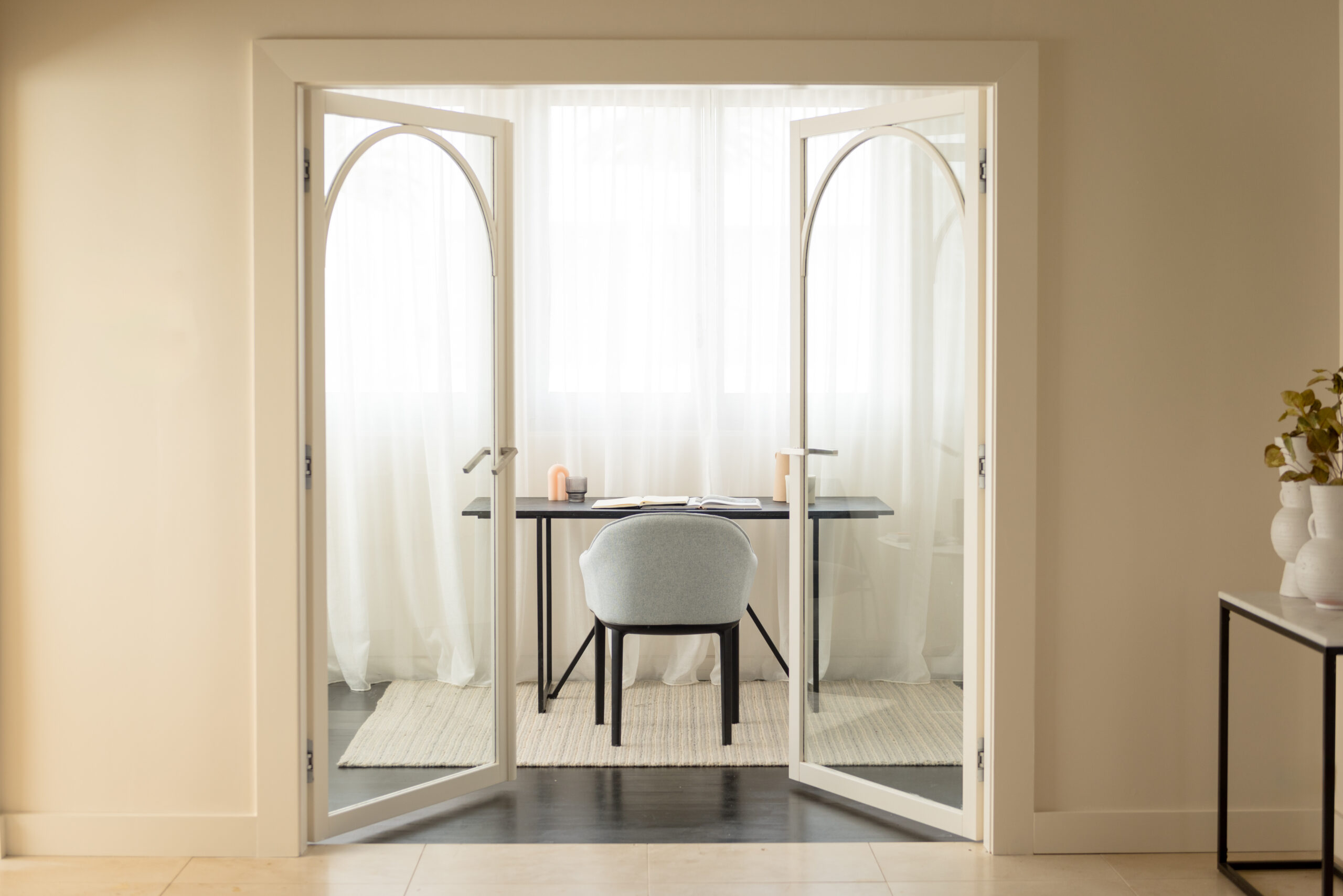 Photo of white double glass doors partially open to the study with a desk, chair and window sheers in the room