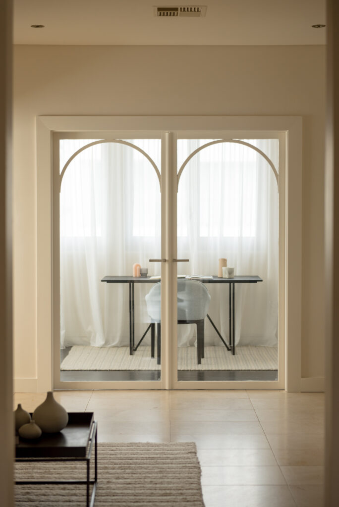 Photo of closed white double glass doors looking into the study with a desk, chair and window sheers in the room