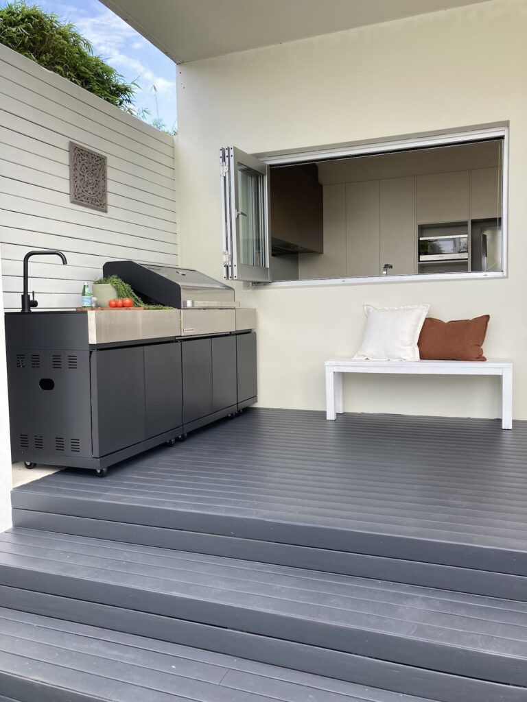 Image of the back porch with outdoor kitchen, bench and servery window open from the kitchen