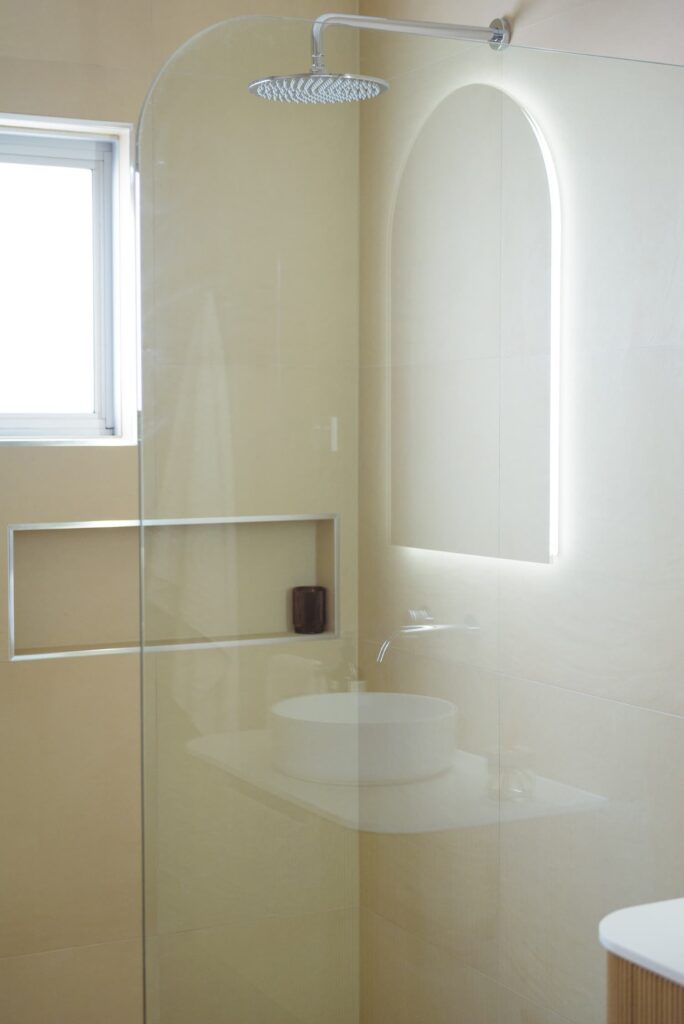 Arched LED mirror, vanity with lighting underneath and an arched shower screen with chrome tapware