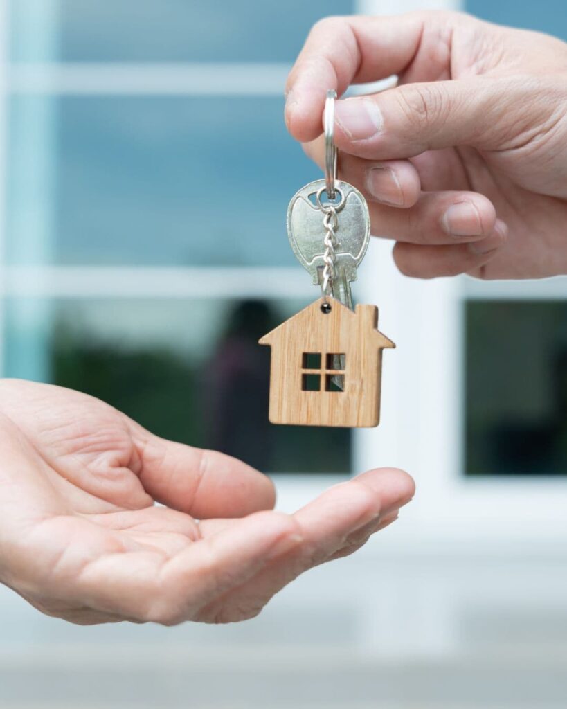 Stock image of a person handing a key with a house keychain on it to another person to show off selling and buying a home